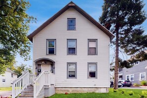 Une maison à deux étages avec un porche à l’avant, un petit escalier et une pelouse bien entretenue.
