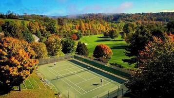 A tennis court surrounded by trees and a golf course in the background.