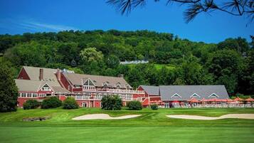 A large red building with multiple stories and a prominent roofline, surrounded by lush green grass and trees.
