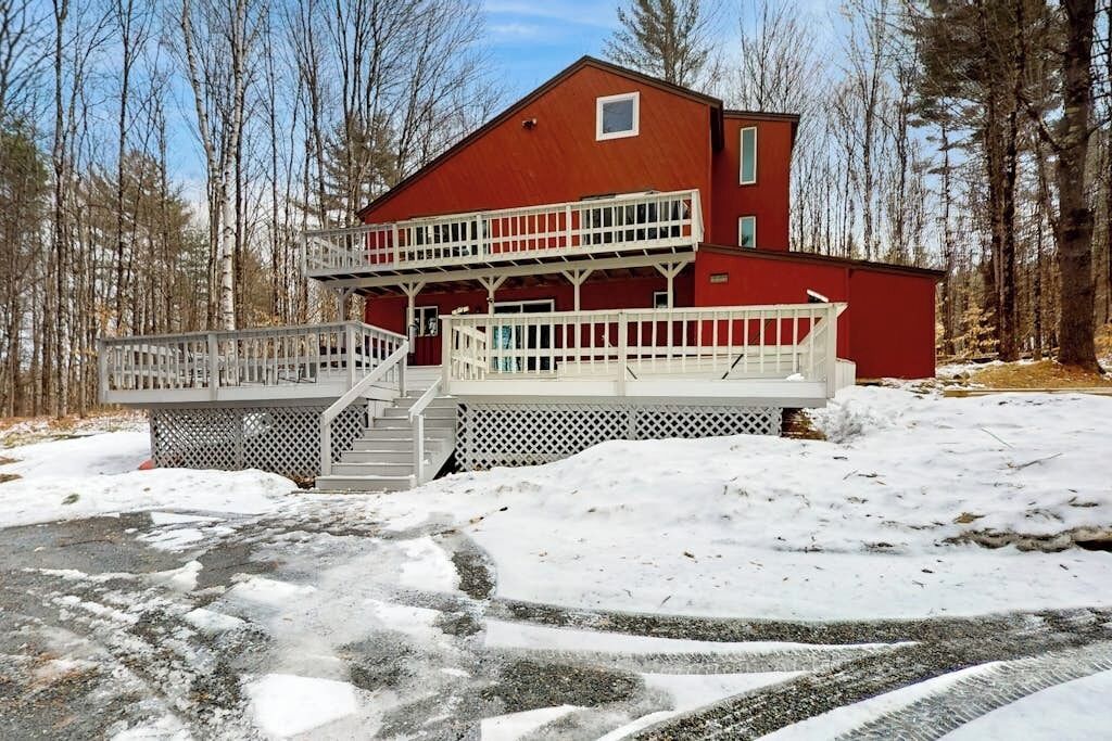 Une cabane à deux étages avec un balcon, entourée de neige et d’arbres.