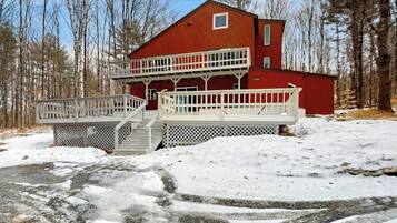 A two-story cabin with a balcony, surrounded by snow and trees.