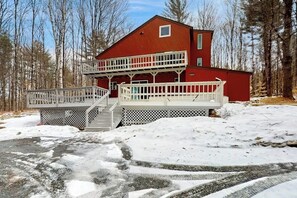 A two-story cabin with a balcony, surrounded by snow and trees.