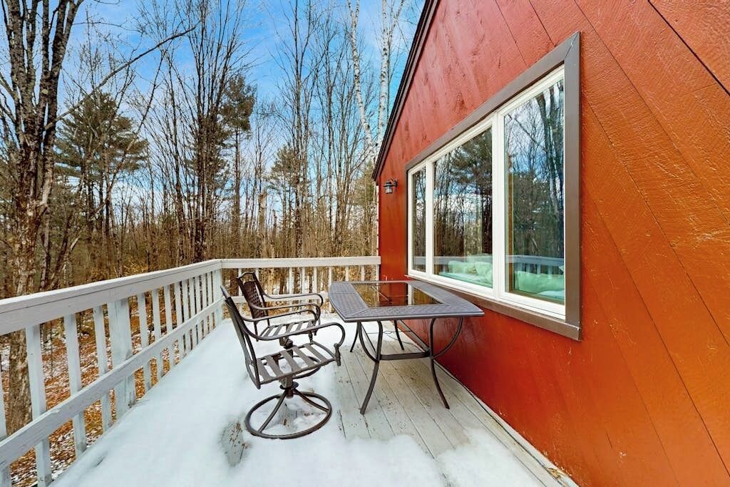Une terrasse en bois avec une table et des chaises, une rambarde et une grande fenêtre.