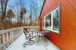 A wooden deck with a table and chairs, a railing, and a large window.