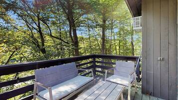 A wooden deck with two white benches and a small table, surrounded by trees.