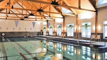 An indoor swimming pool with a wooden ceiling, clear lanes, and lounge chairs.
