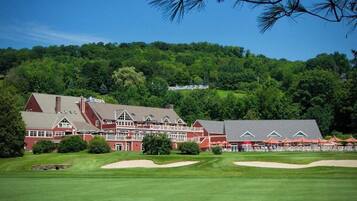 A large building with multiple stories and a red roof, surrounded by a well-maintained lawn and a forested hill in the background.