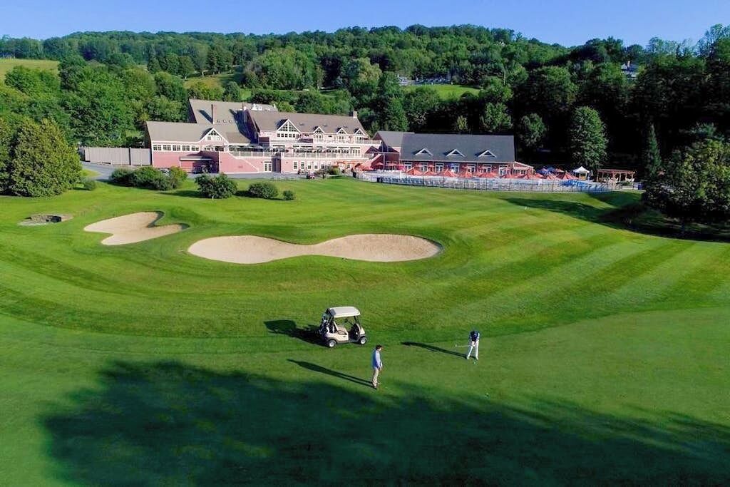 Un parcours de golf doté d’un club-house, de bunkers de sable et offrant une vue sur un ciel dégagé.