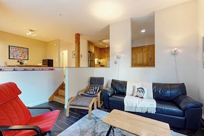 A living room with a sofa, two chairs, a coffee table, and a kitchen in the background. - End-unit condo w/ fireplace, pool, sauna, tennis, deck, ski locker, w/d (Waitsfield)
