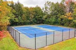 A tennis court with a net, surrounded by a fence, and trees in the background.