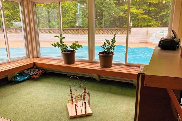 A room with large windows, a wooden bench, two potted plants, and a beaded toy on the floor.