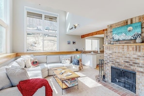 A modern living room with a sectional sofa, a fireplace, and large windows. - Mountain-view home with new deck, fireplace, & shared pool - walk to lifts (Warren)