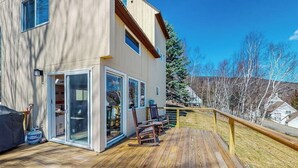 A two-story building with a wooden deck, sliding glass doors, and a view of a snowy landscape. - Mountain-view home with new deck, fireplace, & shared pool - walk to lifts (Warren)