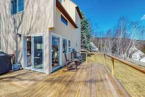 A two-story building with a wooden deck, sliding glass doors, and a view of a snowy landscape. - Mountain-view home with new deck, fireplace, & shared pool - walk to lifts (Warren)