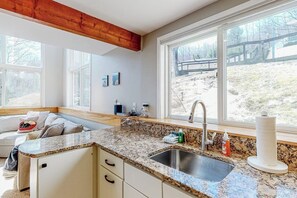 A kitchen with a granite countertop, stainless steel sink, and a window with a view of a wooden deck. - Mountain-view home with new deck, fireplace, & shared pool - walk to lifts (Warren)