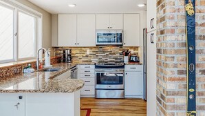 A modern kitchen with white cabinets, a microwave, a stove, and a brick wall. - Mountain-view home with new deck, fireplace, & shared pool - walk to lifts (Warren)