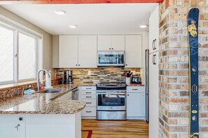 A modern kitchen with white cabinets, a microwave, a stove, and a brick wall. - Mountain-view home with new deck, fireplace, & shared pool - walk to lifts (Warren)