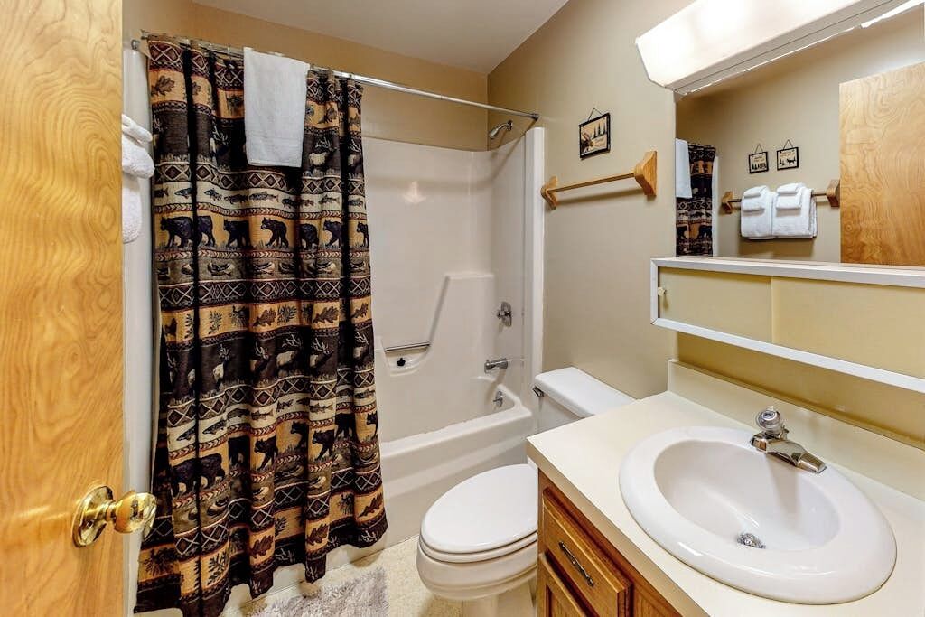 A bathroom with a shower, toilet, sink, and wooden vanity.
