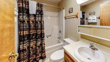 A bathroom with a shower, toilet, sink, and wooden vanity.