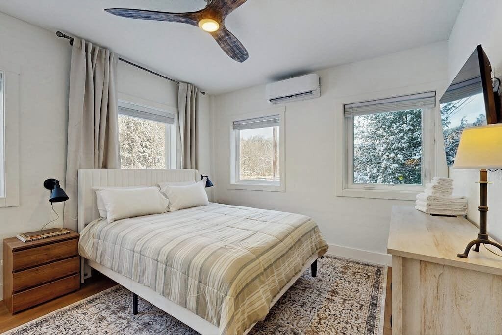 Ein Schlafzimmer mit Bett, Nachttischen, Deckenventilator, Fenstern und einer Lampe.