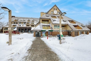 A multi-story hotel with a snow-covered entrance and a visible clock on the building. - Top-Floor Condo w/ view of Killington ski slopes, shared pool, hot tub, sauna (Killington)