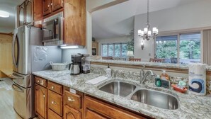 Una cocina con encimeras de granito, electrodomésticos de acero inoxidable, armarios de madera y un amplio ventanal con vista a árboles.