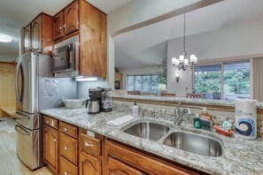 Una cocina con encimeras de granito, electrodomésticos de acero inoxidable, armarios de madera y un amplio ventanal con vista a árboles.