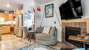 Ein Wohnzimmer mit Sofa, Fernseher, Kamin und Küchenzeile.