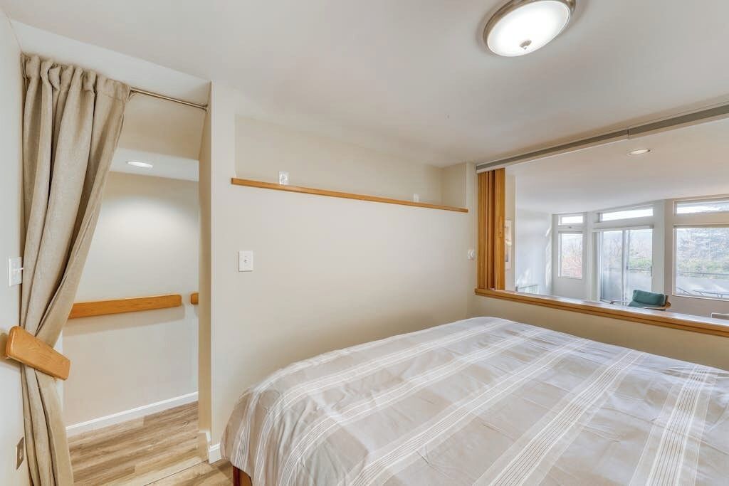 Un dormitorio con cama, ventana, estante de madera y puerta con cortinas.