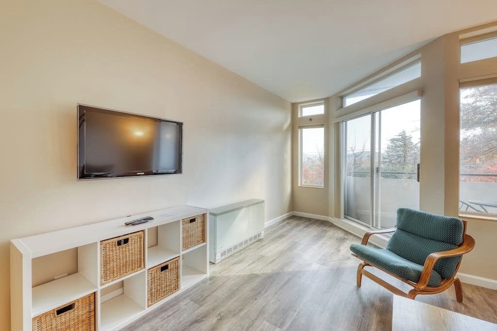 Uma sala de estar moderna com uma televisão de tela plana, uma cadeira de madeira e um console branco com cestos.