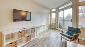 Un salon moderne avec un téléviseur à écran plat, une chaise en bois et une console blanche agrémentée de paniers.