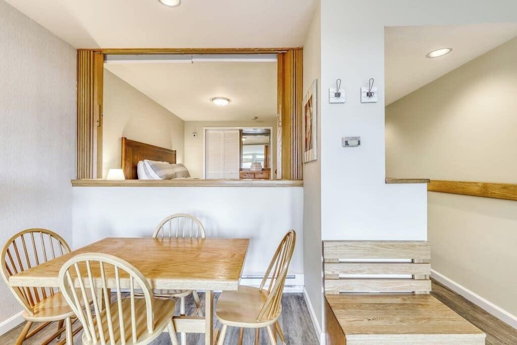 Uma área de refeições com uma mesa e cadeiras de madeira, um espelho sobre a mesa e uma escada que leva a outro quarto.