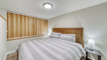 Un dormitorio con cama, mesita de noche, lámpara, cabecera de madera y ventana con persianas.