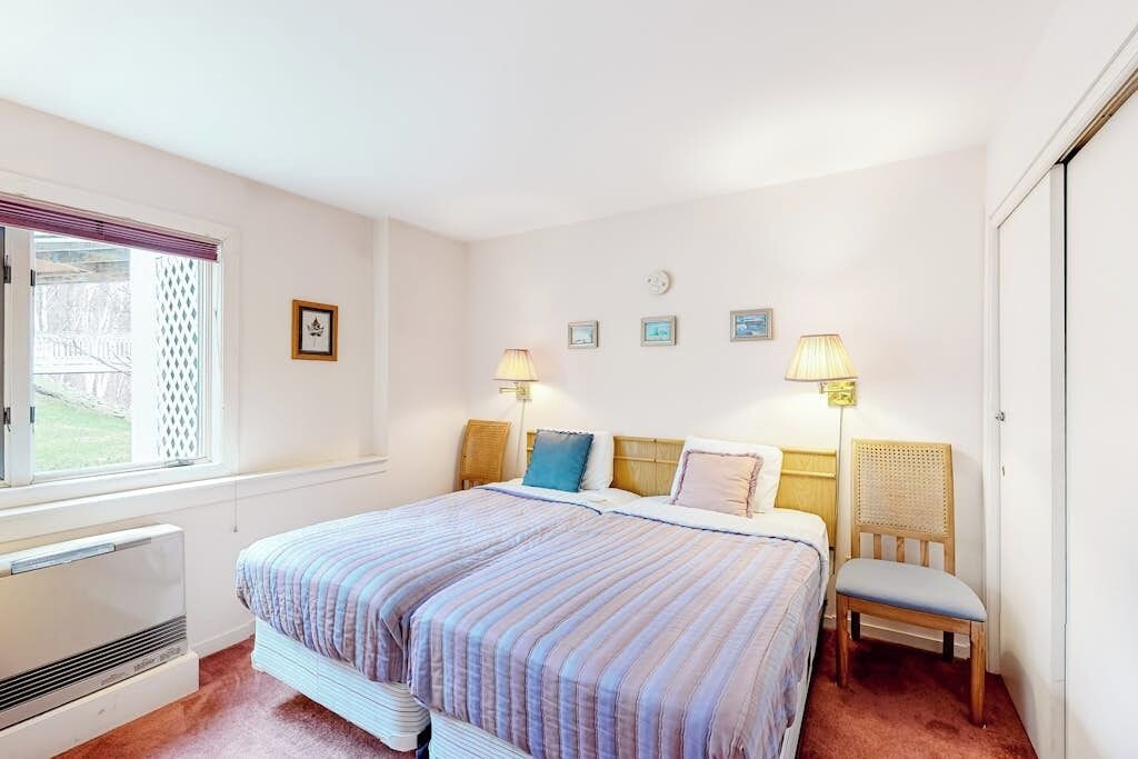 Une chambre à coucher comprenant un lit, des lampes de chevet, une chaise, un radiateur et une fenêtre avec des stores.