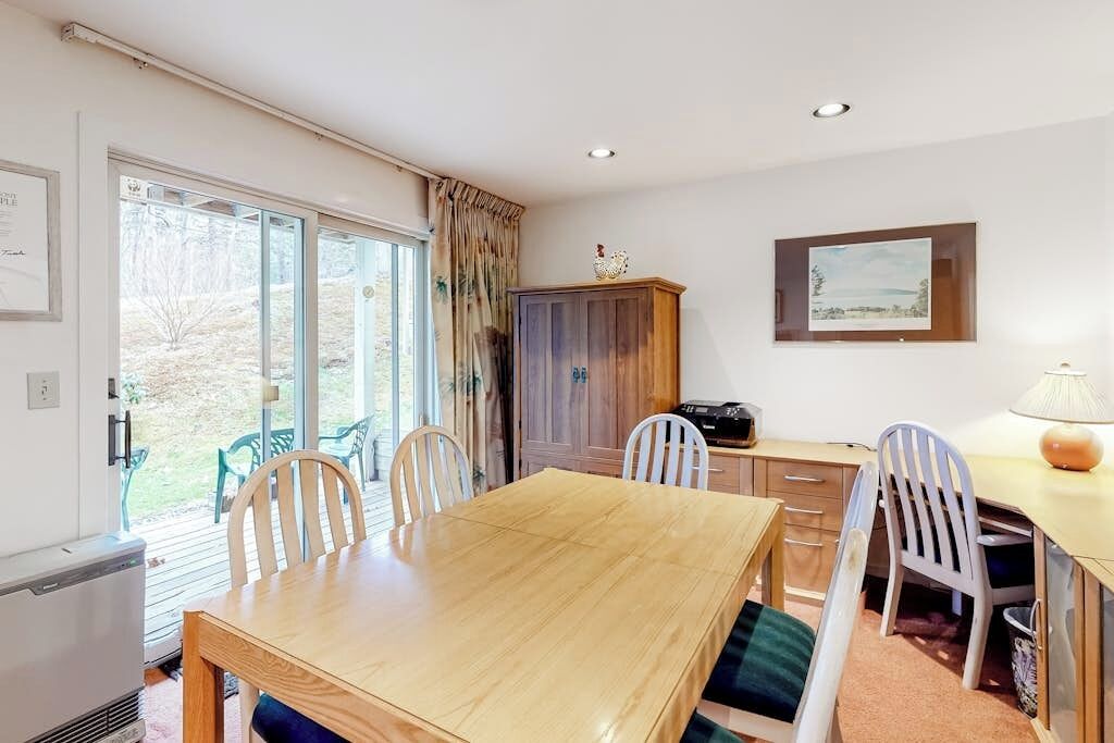 Un espace repas comprenant une table en bois, des chaises, un buffet et un bureau avec une lampe.