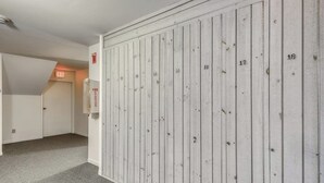 A hallway with a white wooden wall, numbered doors, and an exit sign. - Ski condo with locker, shuttle, fast WiFi, fireplace, washer/dryer & AC (Warren)