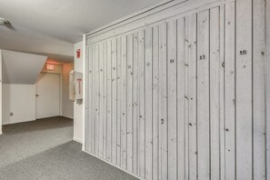 A hallway with a white wooden wall, numbered doors, and an exit sign. - Ski condo with locker, shuttle, fast WiFi, fireplace, washer/dryer & AC (Warren)