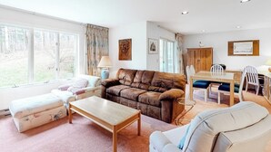 A spacious living room with a brown leather sofa, a white armchair, a wooden coffee table, and a dining area with a wooden table and chairs. - Ski condo with locker, shuttle, fast WiFi, fireplace, washer/dryer & AC (Warren)