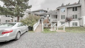A multi-story residential building with a driveway, a car parked on the left, and a staircase leading to the entrance. - Ski condo with locker, shuttle, fast WiFi, fireplace, washer/dryer & AC (Warren)