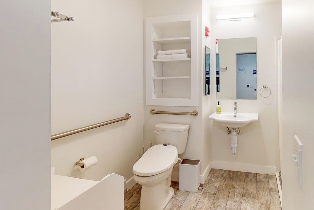 A bathroom with a toilet, a sink, a mirror, and a shelf with towels.