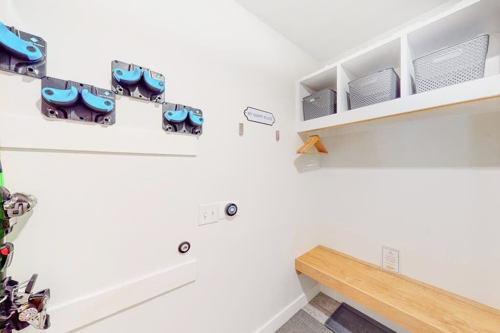 Ein helles, modernes Badezimmer mit weißer Wand, einer Holzbank und einem Regal mit Aufbewahrungsboxen.