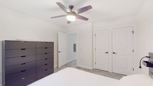 Een slaapkamer met een bed, een kaptafel, een plafondventilator en witte deuren.