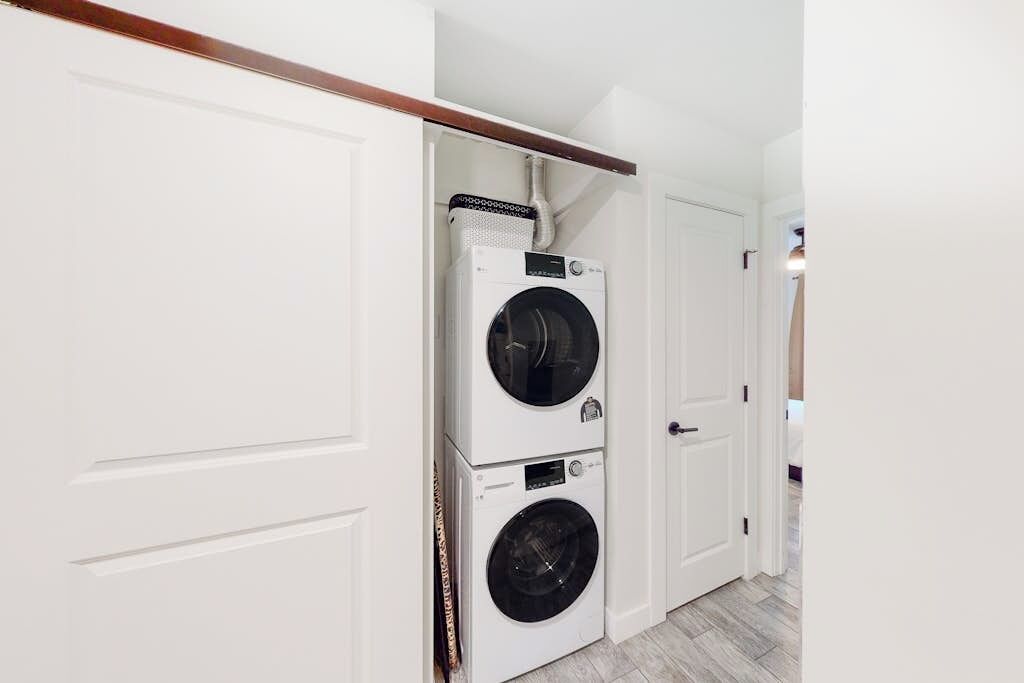 A laundry room with two stacked washing machines, a white door, and a wooden ceiling beam.