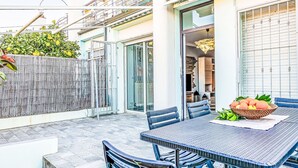 Een terras met een tafel en stoelen, een mand met fruit en uitzicht op een gebouw met een glazen deur.