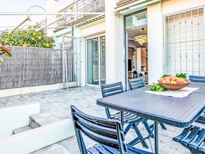 Eine Terrasse mit Tisch und Stühlen, einem Obstkorb und Blick auf ein Gebäude mit Glastür.