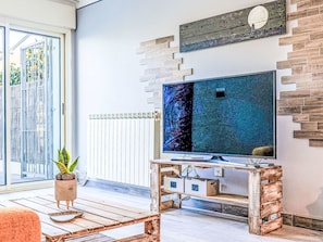 Ein Wohnzimmer mit Fernseher auf Holzfuß, einer Topfpflanze und Blick durch eine Glastür.