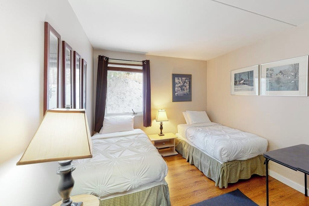 A hotel room with two beds, a desk, a lamp, and framed pictures on the wall.