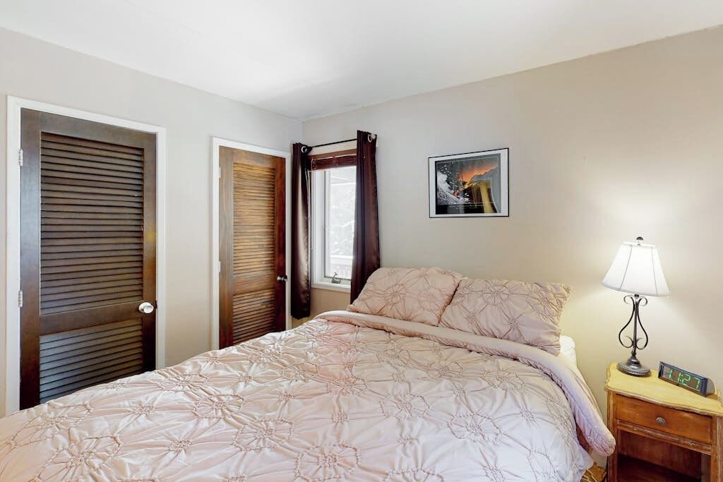 Een slaapkamer met een bed, een nachtkastje met een lamp, een lijst aan de muur en twee deuren.