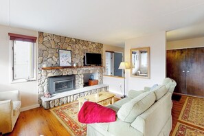 A living room with a stone fireplace, a sofa, a television, and a wooden floor.