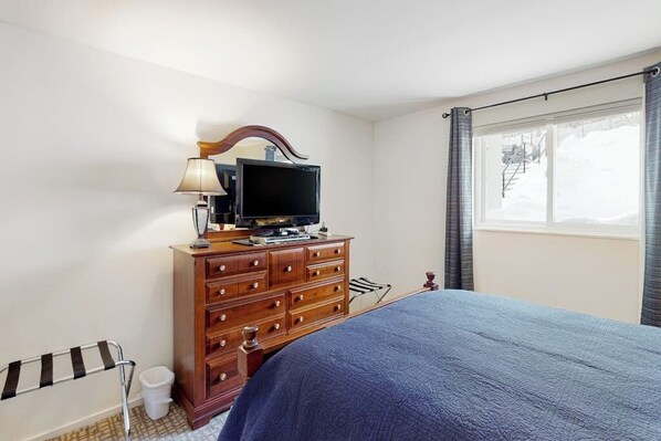 A bedroom with a bed, a dresser, a television, a window with curtains, and a radiator. - First-floor Sugarbush Village condo with fireplace and ski locker, walk to lift (Warren)